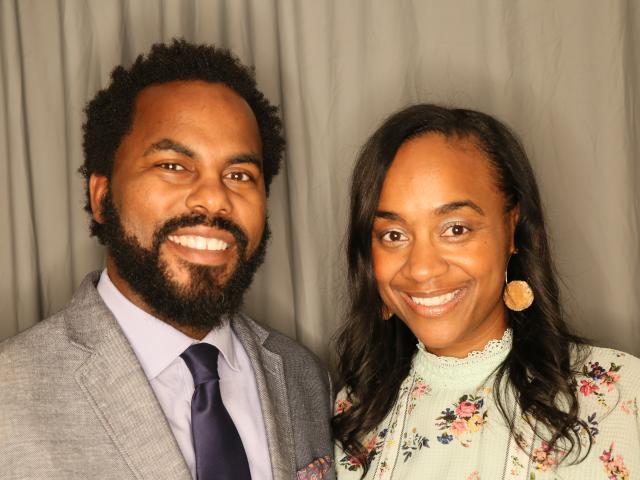 Faculty Director Maisha T. Winn and Executive Director Lawrence "Torry" Winn smiling, next to each other behind a gray curtain background.