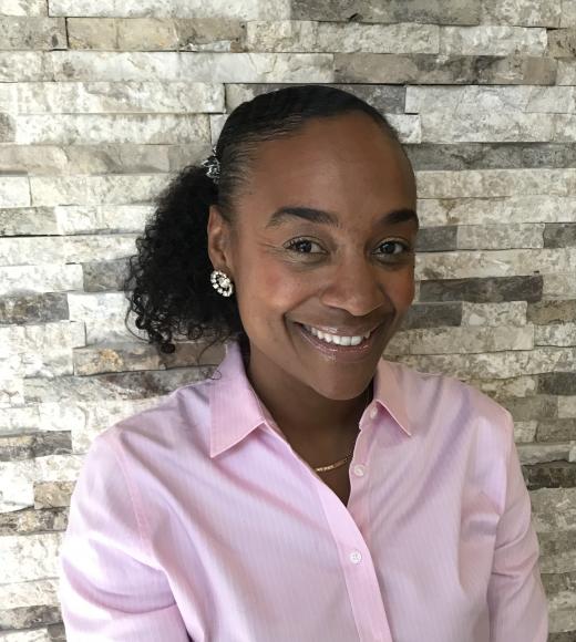 Maisha Winn smiling in a pink button-up blouse with flower earring facing camera